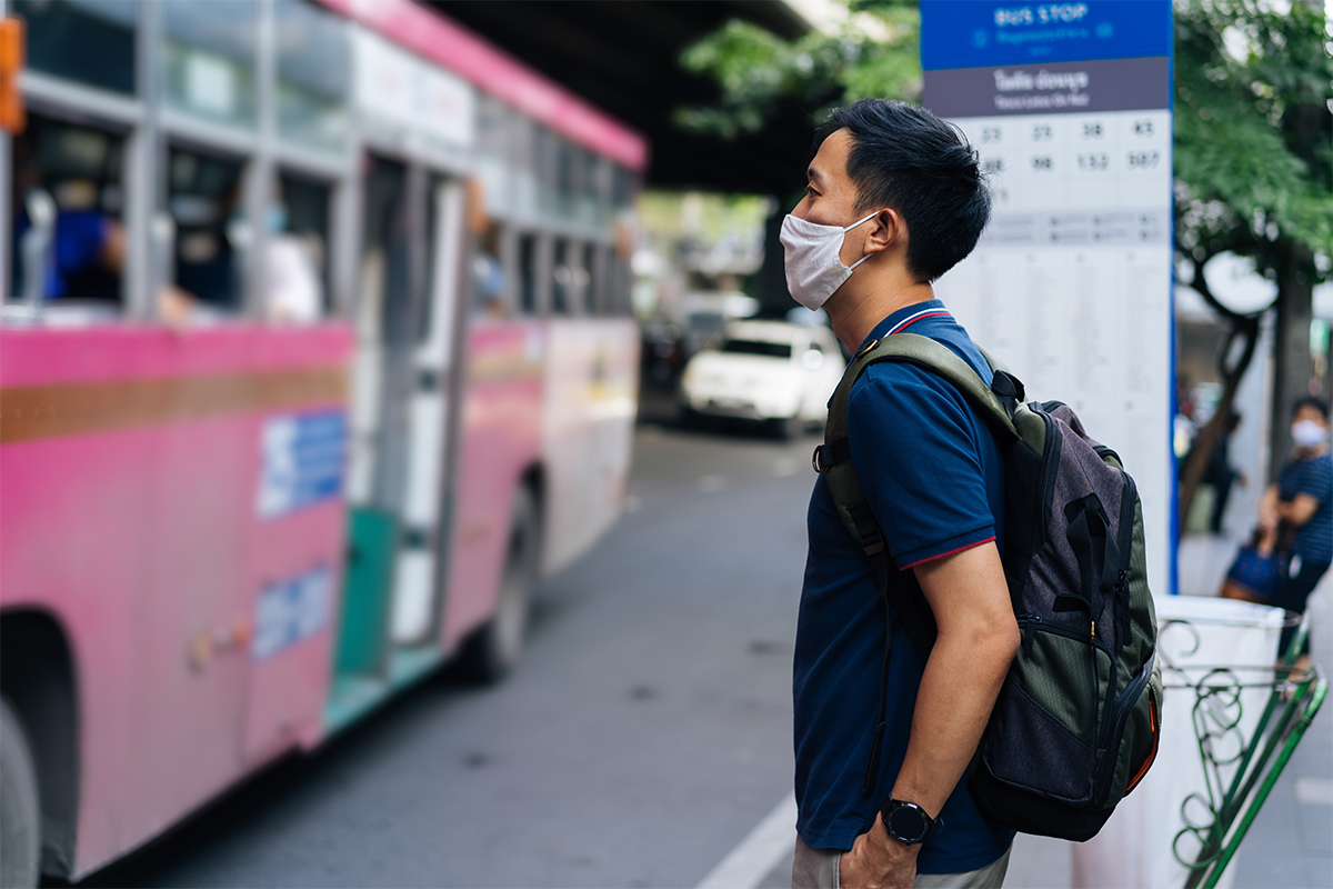 Image of adult man waiting for bus while wearing a face mask. 